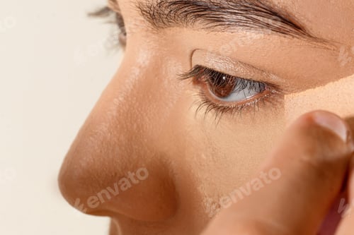 Preview: Closeup shot of a person's hand using a sponge to spread the foundation on a woman's skin.