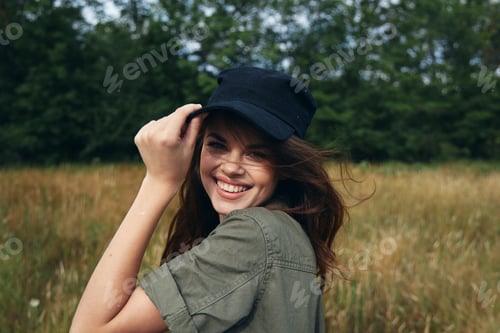 Preview: A woman straightens her cap on her head and laughs outdoors