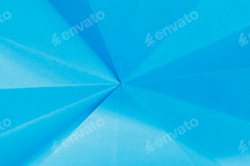 Preview: Bright blue paper folded into a geometric pattern on a flat surface during daytime