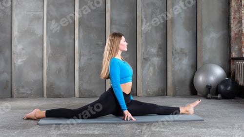 Preview: A young athletic woman is sitting on a splits on a yoga mat. Stretching, yoga and Pilates.