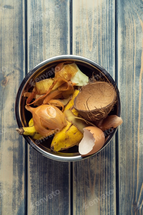 Preview: Metal bowl full of organic food scraps and peel rubbish on wooden background. Overconsumption and