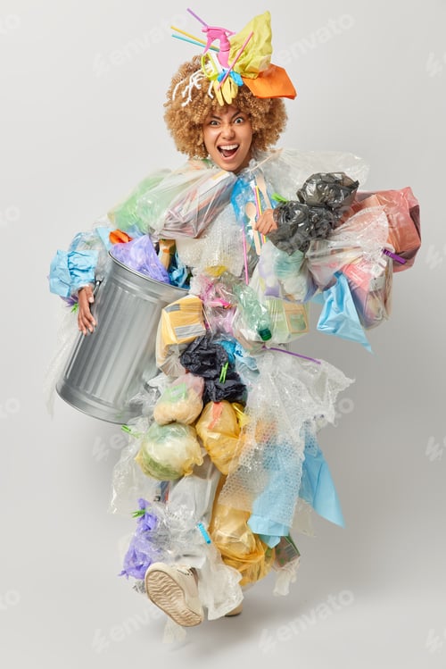 Preview: Vertical shot of annoyed woman covered with plastic litter collects rubbish for recycling carries bi