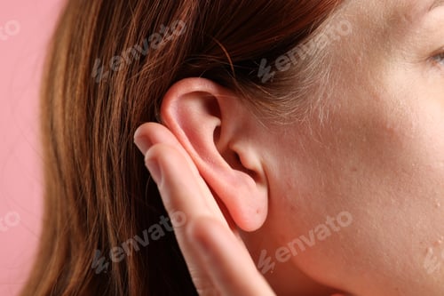 Preview: Sound. Woman showing hand to ear gesture on pink background, closeup
