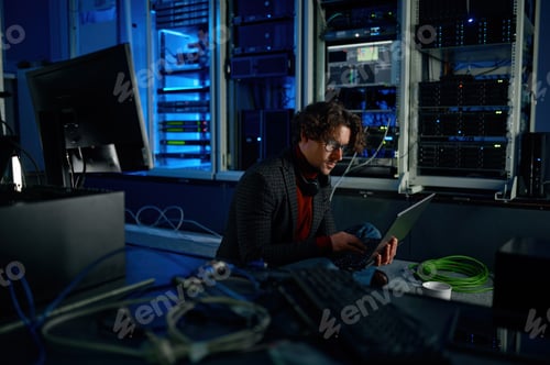 Preview: Male system administrator working in server room using laptop