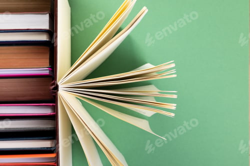 Preview: Books and notebooks in row with opened notebook on top and copy space on green background