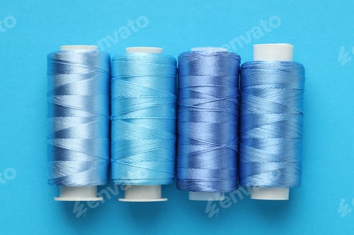 Preview: Spools of sewing threads on light blue background, flat lay