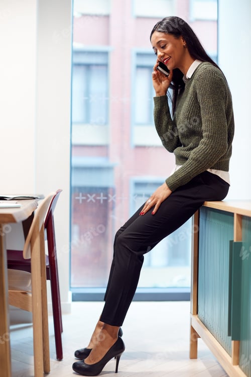 Preview: Businesswoman Sitting On Desk In Meeting Room Talking On Mobile Phone