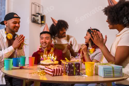 Preview: Multi-ethnic group of friends at a birthday party at home applauding before blowing out the candles