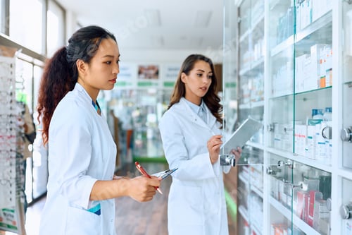 Preview: Chinese pharmacist and her female colleague going through medicine inventory in a pharmacy.