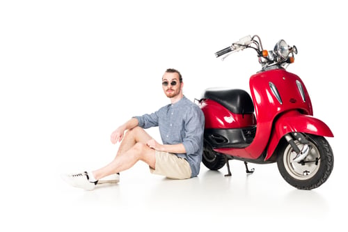 Preview: handsome stylish young man sitting near red scooter isolated on white