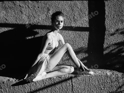 Preview: Graceful young woman sitting elegantly on a stone wall with legs crossed in black and white