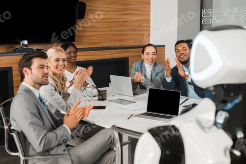 Preview: selective focus of multicultural businesspeople applauding while looking at robot in office