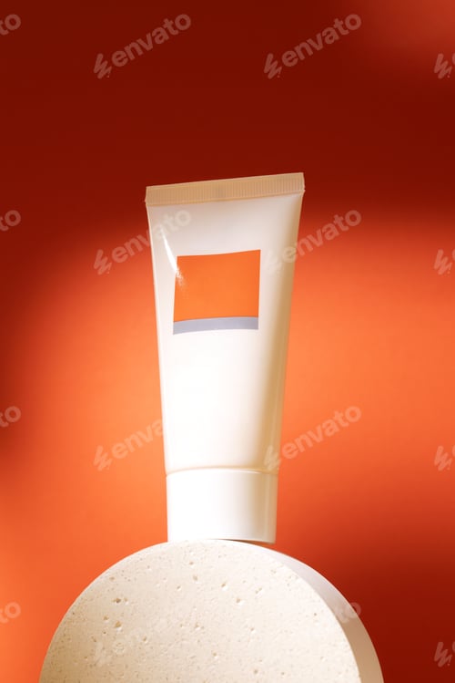 Preview: White plastic tube with face, hand and body cream on podium on orange background with shadow.