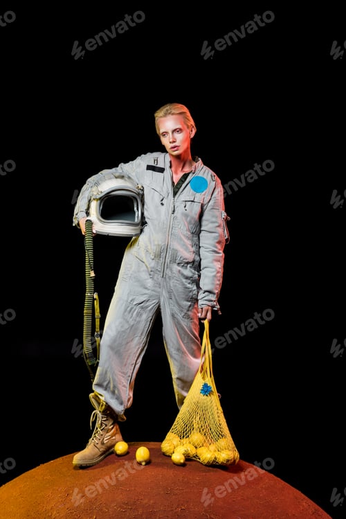 Preview: attractive cosmonaut in spacesuit with helmet and lemons in string bag posing on mars