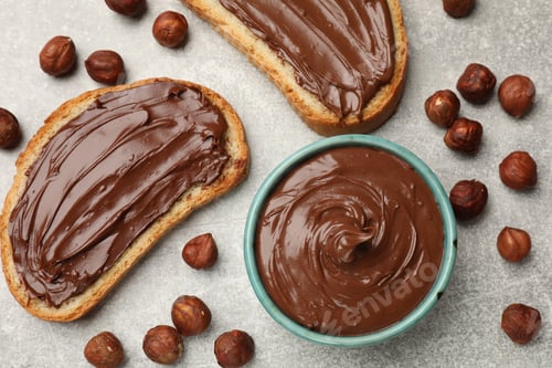 Preview: Toasts with tasty chocolate hazelnut spread and nuts on grey table, flat lay