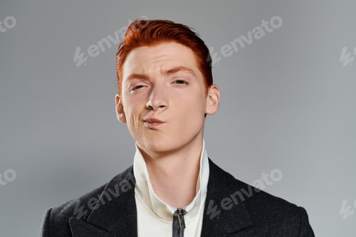 Preview: Stylish young man with vibrant red hair poses confidently against a grey backdrop