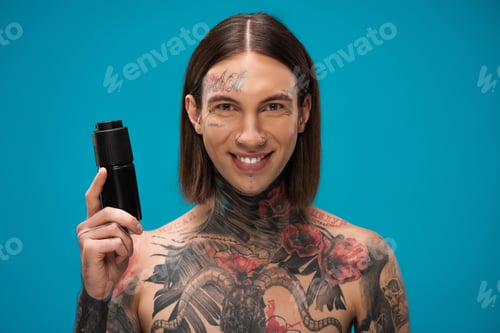 Preview: happy and tattooed young man holding antiperspirant isolated on blue