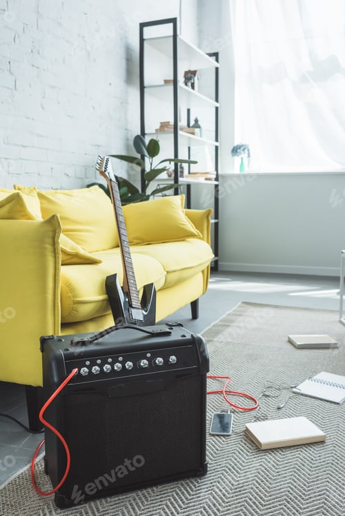 Preview: electric guitar and loud speaker with smartphone standing on floor with books near sofa