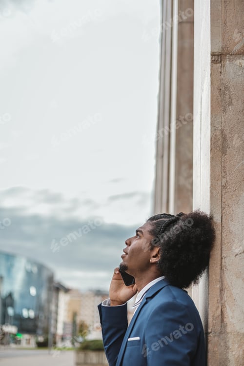 Preview: Young afro man in blazer with mobile phone looking up to the sky. Sky background