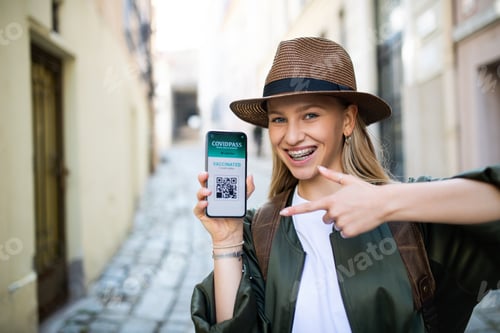 Preview: Young woman traveler in city on holiday showing covid-19 vaccine passport on smartphone