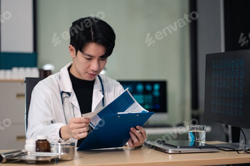 Preview: Male doctor working on desk with laptop computer and paperwork in the office.