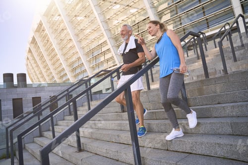 Preview: Middle aged couple, man and woman in sportswear walking down the stairs after exercising together