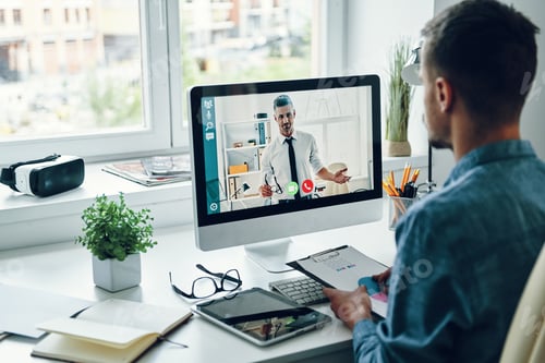 Preview: Serious young man talking to collegue by video call while sitting in office