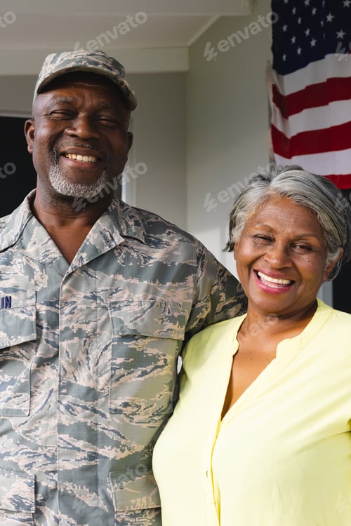 Preview: Portrait of african american military senior man in camouflage clothing with wife against house