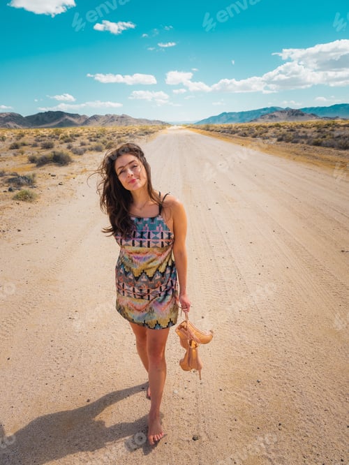 Visualização: Mulher elegante andando pelo deserto com os pés descalços em um vestido enquanto carregava seus sapatos
