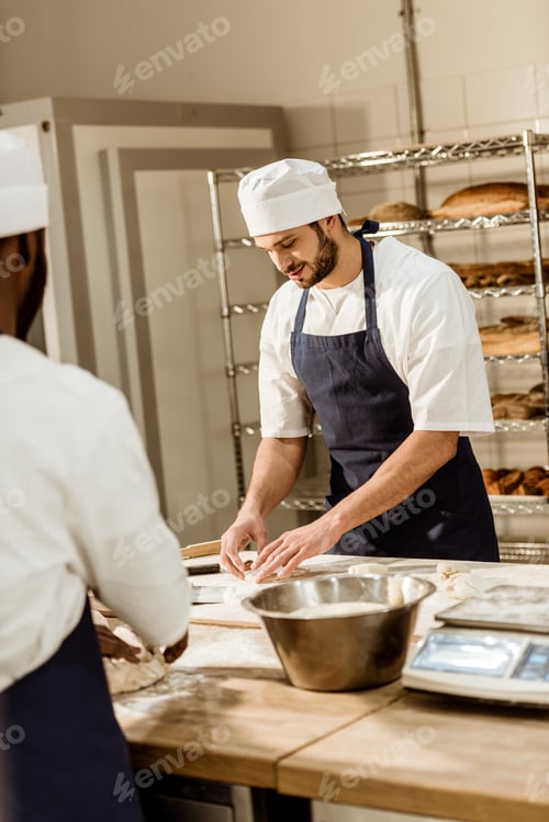 Preview: handsome bakers kneading dough together at baking manufacture