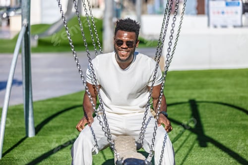 Preview: Smiling man sitting on a swing on the grass in public park