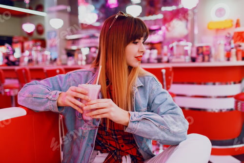 Preview: Fashionable girl in jeans jacket sitting in t retro American cafe.