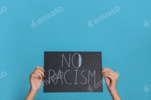 Preview: Woman holding sign with phrase No Racism on light blue background, closeup