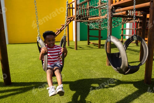 Preview: Playful schoolboy playing on a swing at school playground
