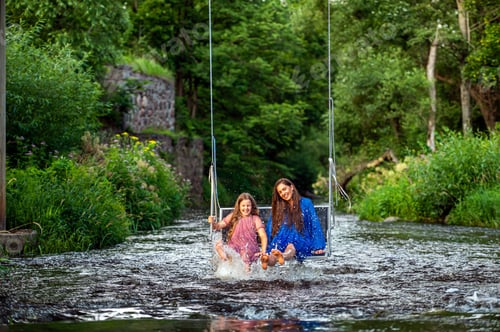 Preview: a woman and a young girl are swinging across a fast-flowing river, laughing and splashing with water