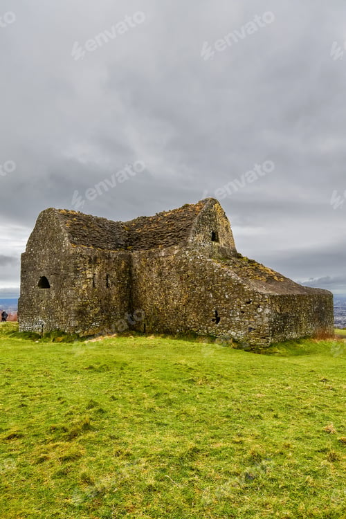 Preview: Old stone building on a lush, grass-covered hill, with a cloudy sky in the background