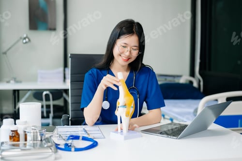 Preview: Confident young Asian female doctor in white medical uniform sit at desk working on computer.