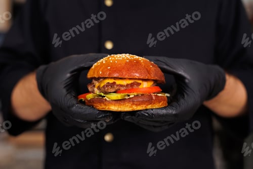 Preview: Cook in black gloves holds a burger in his hands and shows an ok sign.