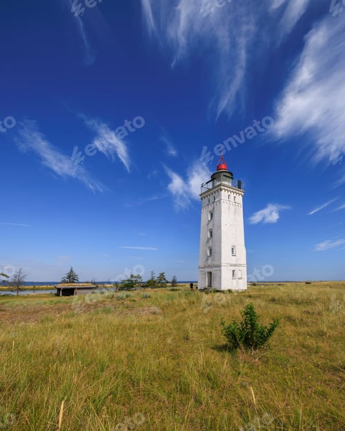 Preview: Scenic view of a white lighthouse standing tall on lush green grass on a sunny day