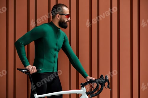 Preview: Portrait of bearded guy with bicycle posing over orange wall background.