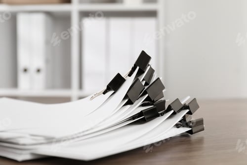 Preview: Binder clips with sheets of paper on wooden table indoors, closeup