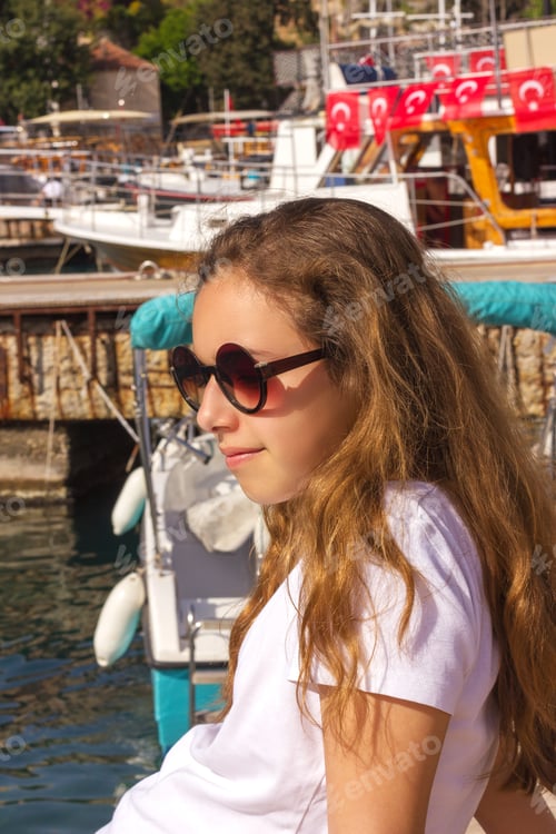 Preview: Young girl with long hair sits on the pier in the yacht port and looks at blue sea