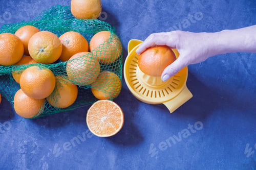 Preview: A woman's hand squeezes juice from an orange, a torn mesh with oranges lies nearby