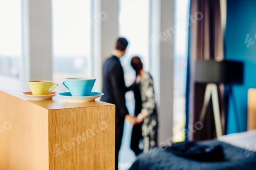 Preview: Close-up of coffee cups on table with couple standing in background at hotel
