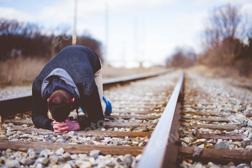 Preview: Closeup shot of a male on the ground on train tracks praying with a blurred background