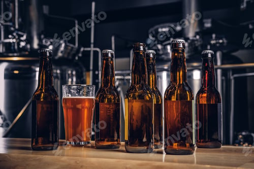 Preview: Bottles and glass of craft beer on wooden bar counter at the indie brewery.