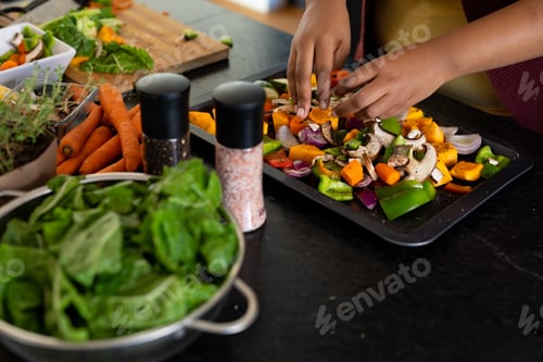 Preview: Midsection of plus size african american woman preparing dinner, seasoning vegetables in kitchen