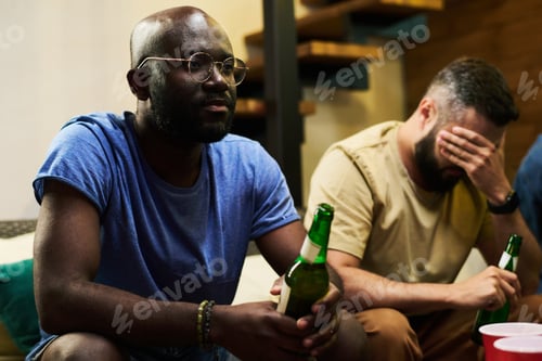 Preview: Young upset African American man with bottle of beer watching football match