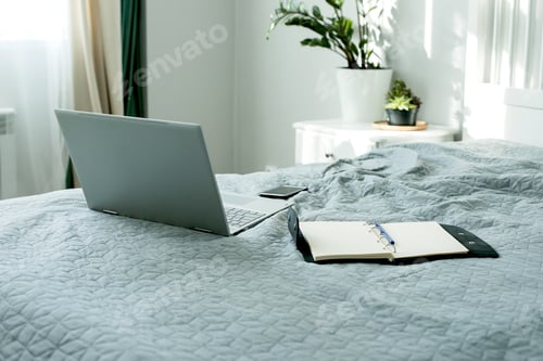 Preview: Laptop, mobile and open notebook on bed. Concept of female business, home education, shopping online