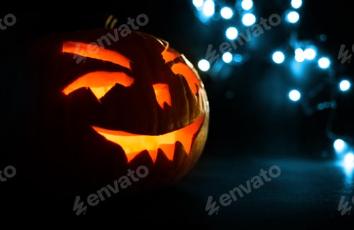 Preview: carved face of pumpkin glowing on Halloween on blue bokeh light background